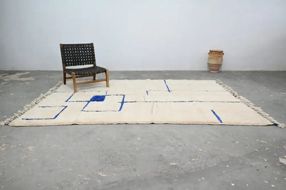 Cream-colored beni ouarain rug with bold blue geometric patterns and fringed edges moroccan handmade traditional design
