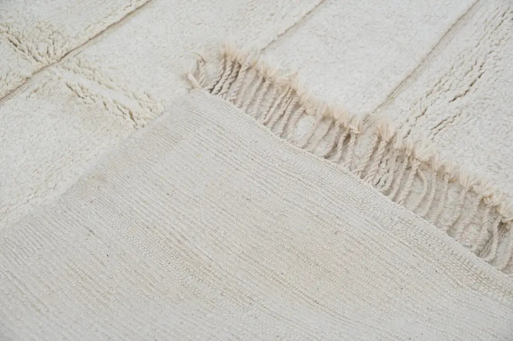 Cream-colored textured wool beni ouarain rug with fringed edges in 303 x 205 cm by DecorBites™