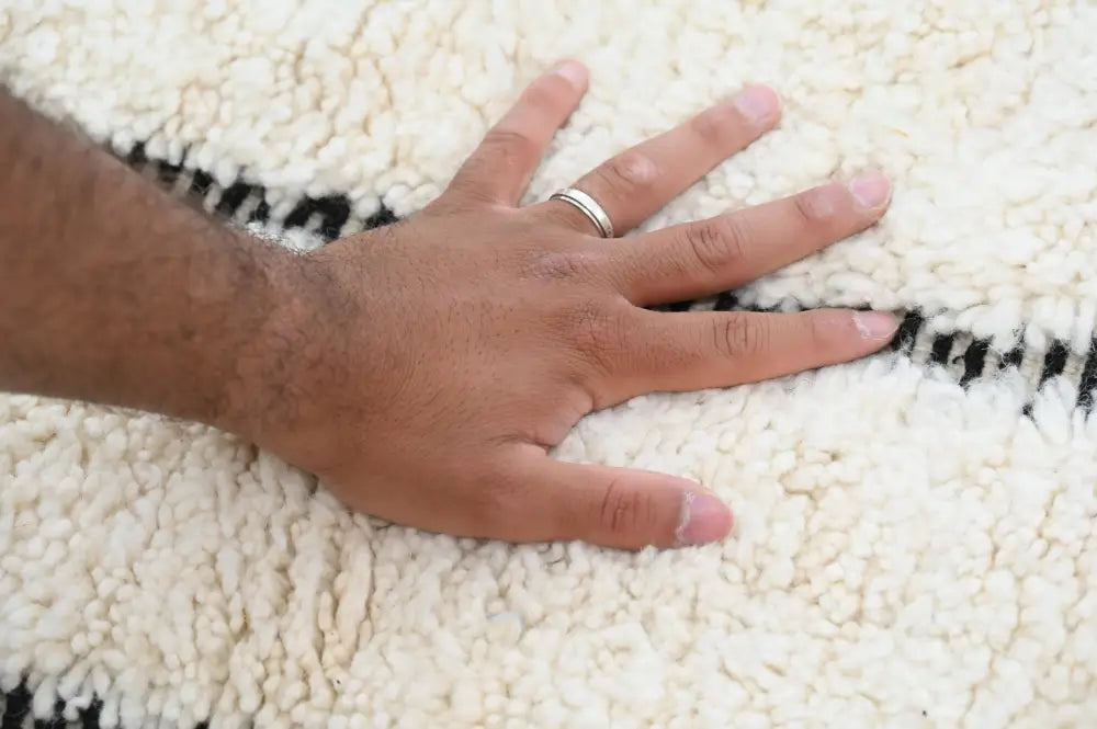 A hand rests on a cream beni ouarain rug with bold black geometric stripes moroccan handmade and plush texture