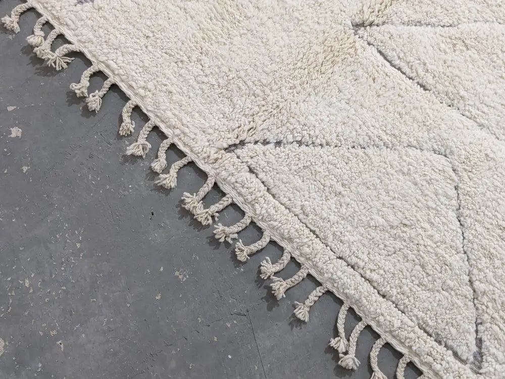 Cream-colored moroccan handmade beni ouarain rug with plush wool texture and decorative tassels on edges 305 x 204 cm