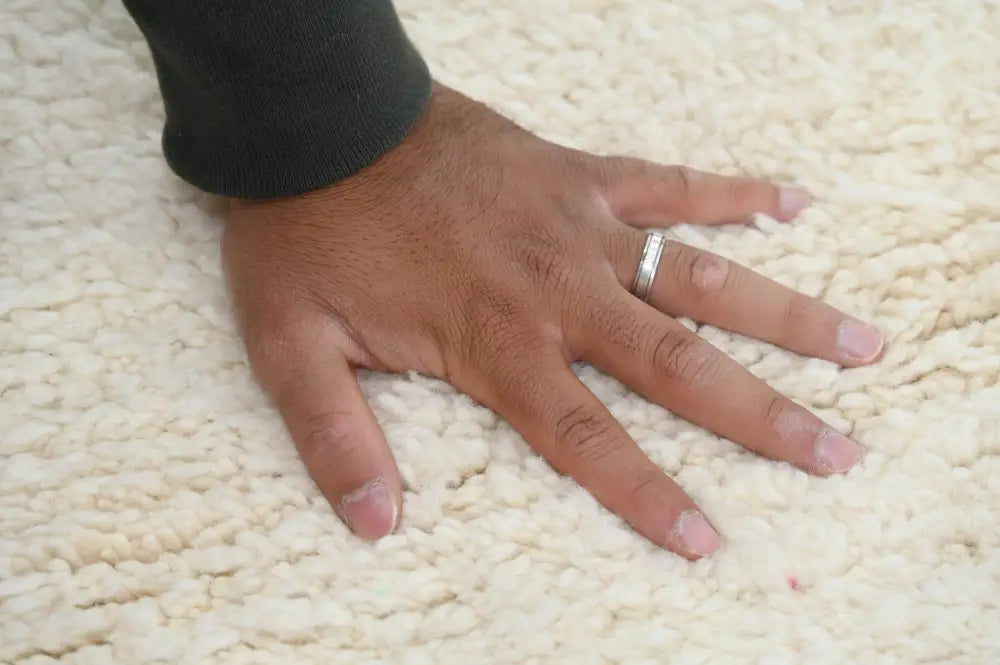 A hand with a silver band touches a cream beni ouarain rug from DecorBites™ Moroccan handmade collection