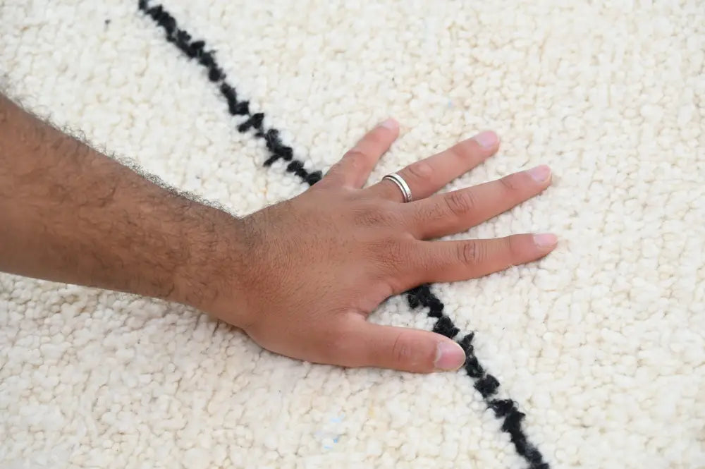 A hand with silver ring rests on cream beni ouarain rug with bold black geometric stripes moroccan handmade decor