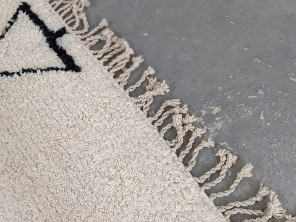 Cream-colored beni ouarain rug with black geometric triangle design and natural fiber fringe moroccan handmade wool rug