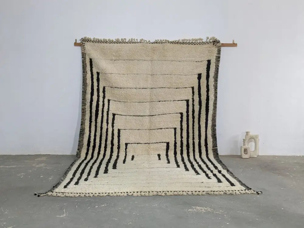 A cream-colored beni ouarain rug with bold black geometric stripes and fringed edges moroccan handmade textile