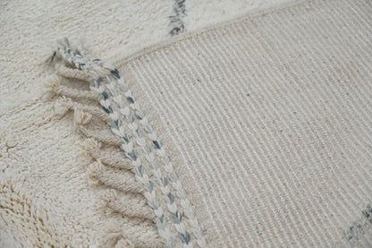 Cream-colored moroccan handmade beni ouarain rug with textured wool surface and fringed edges accented by gray threads