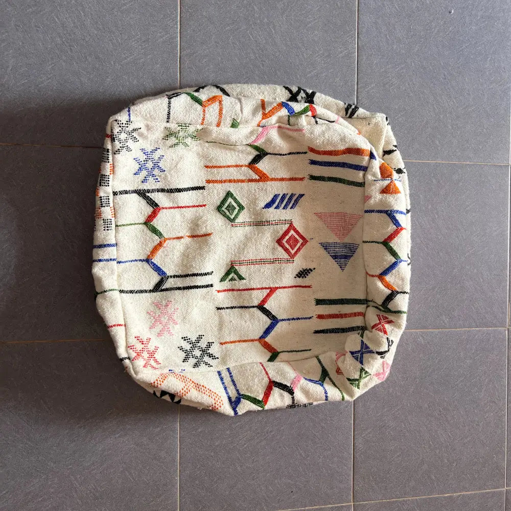 Cream-colored decorbites moroccan handmade pouf 60cm x 60cm with vibrant geometric pattern in red blue green and black