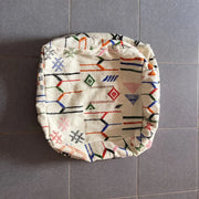 Cream-colored decorbites moroccan handmade pouf 60cm x 60cm with vibrant geometric pattern in red blue green and black