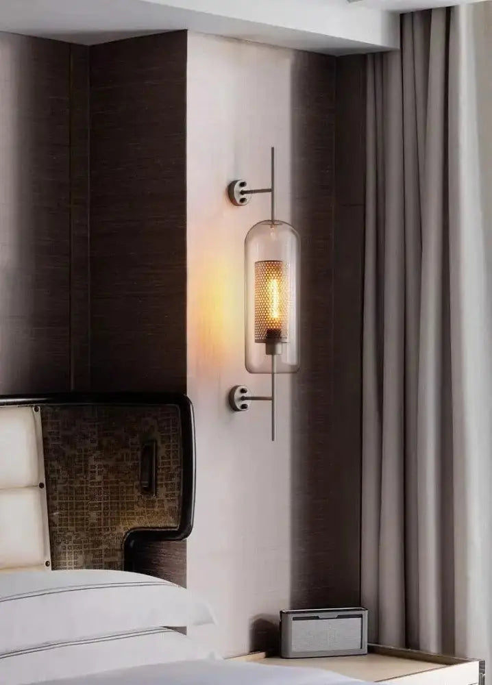 DecorBites Moroccan modern bathroom wall sconce with clear glass cylinder and metallic arms featuring illuminated filament bulb