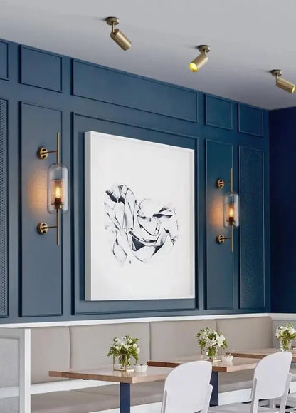 A framed black-and-white abstract artwork on a dark blue paneled wall complements a modern bathroom wall sconce
