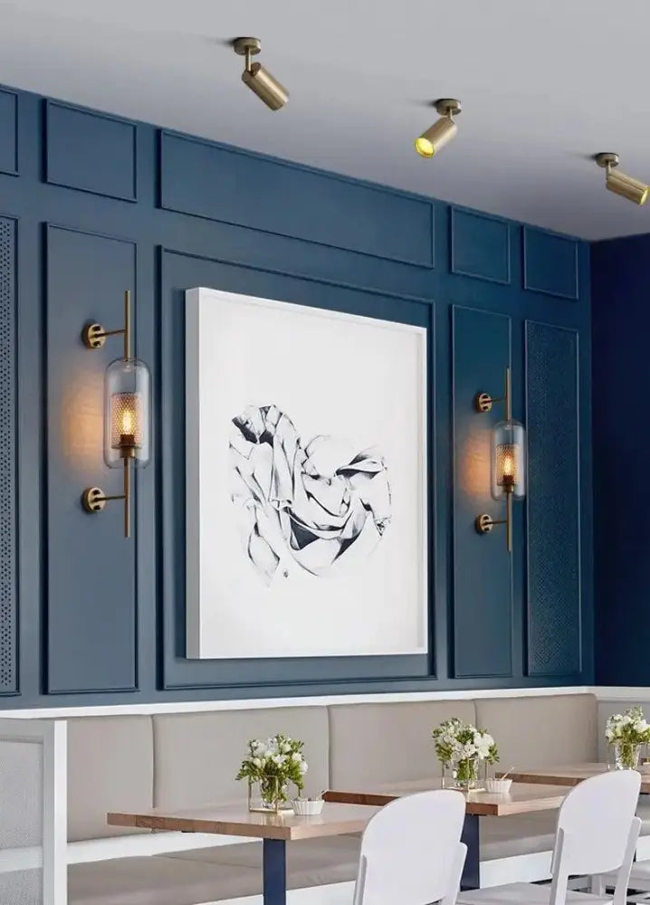 A framed black-and-white abstract artwork on a dark blue paneled wall complements a modern bathroom wall sconce