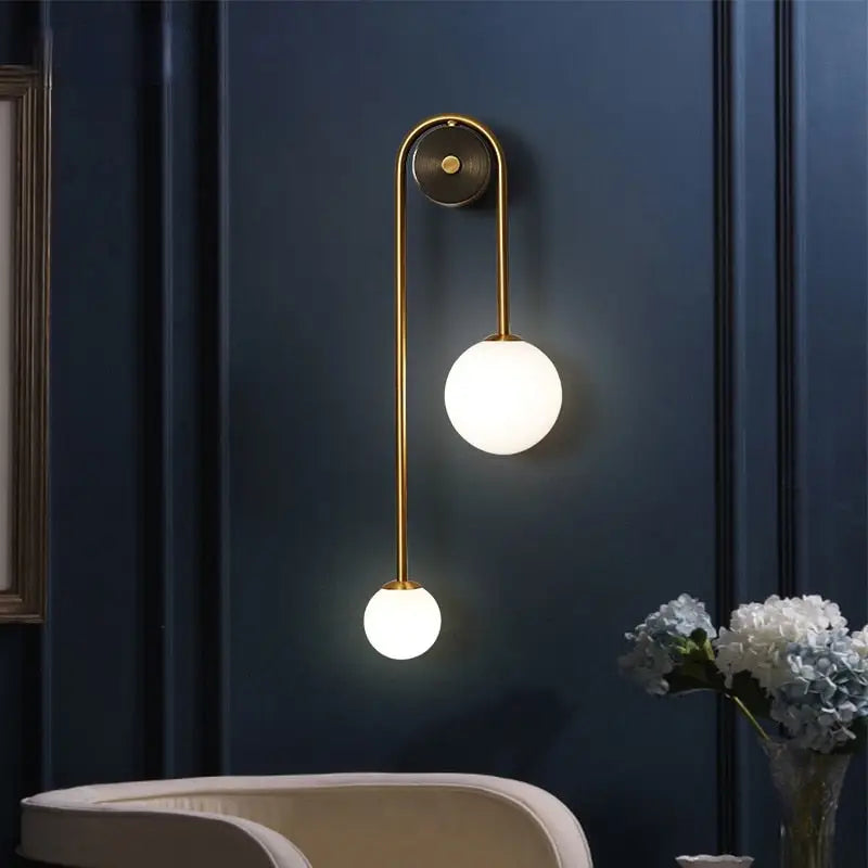 Traditional gold wall sconces featuring gold toned metal arms and two spherical frosted glass globes for elegant lighting