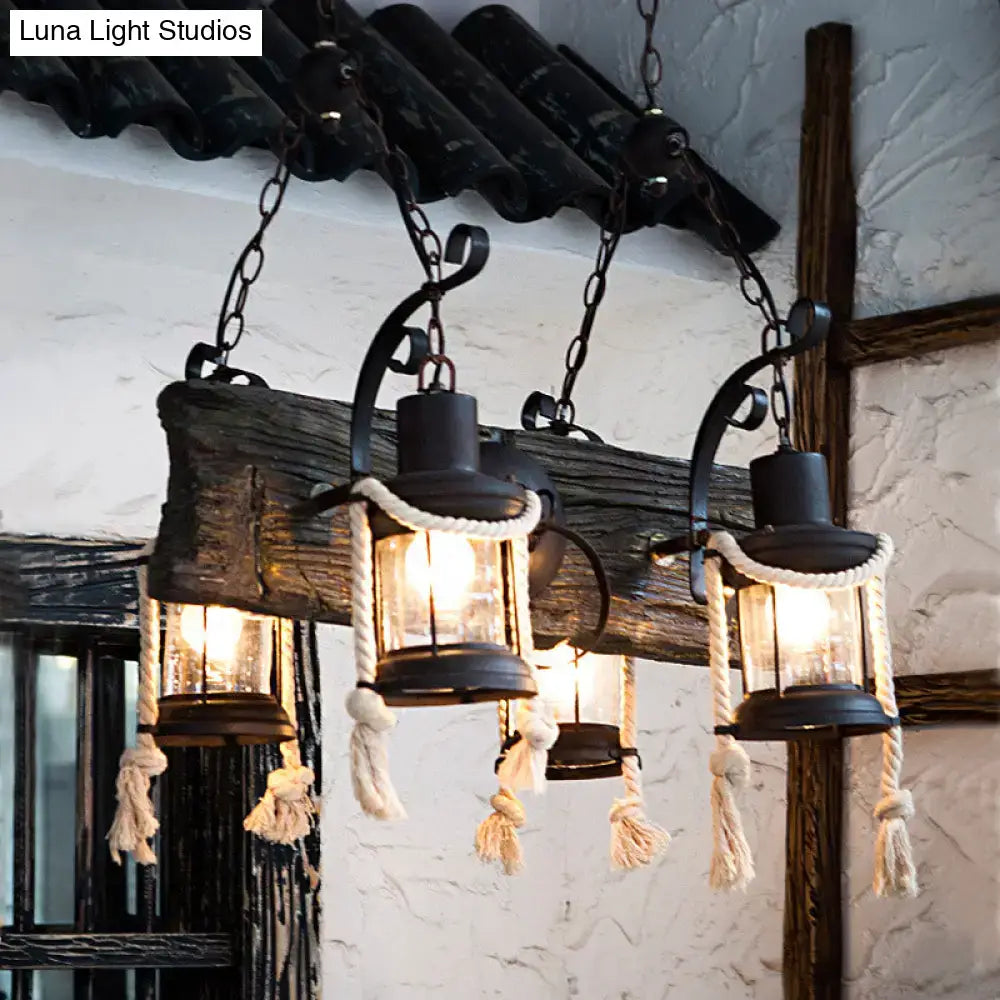 Rustic black metal island lamp with glass panels and hemp rope accents hanging from a weathered wood beam bulb base