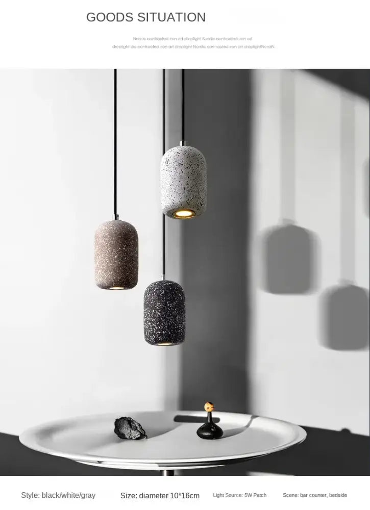 Three cylindrical industrial style cement pendant lamps in black white and gray with speckled concrete finish hanging