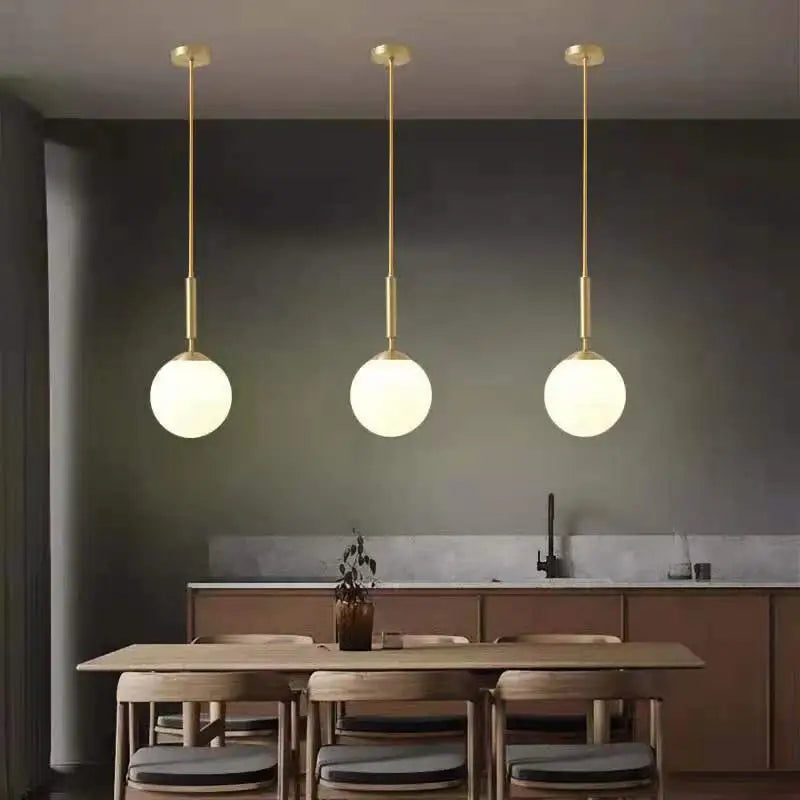 Three DecorBites™ Nordic glass ball pendant lights with gold metal rods and frosted shades above wooden table