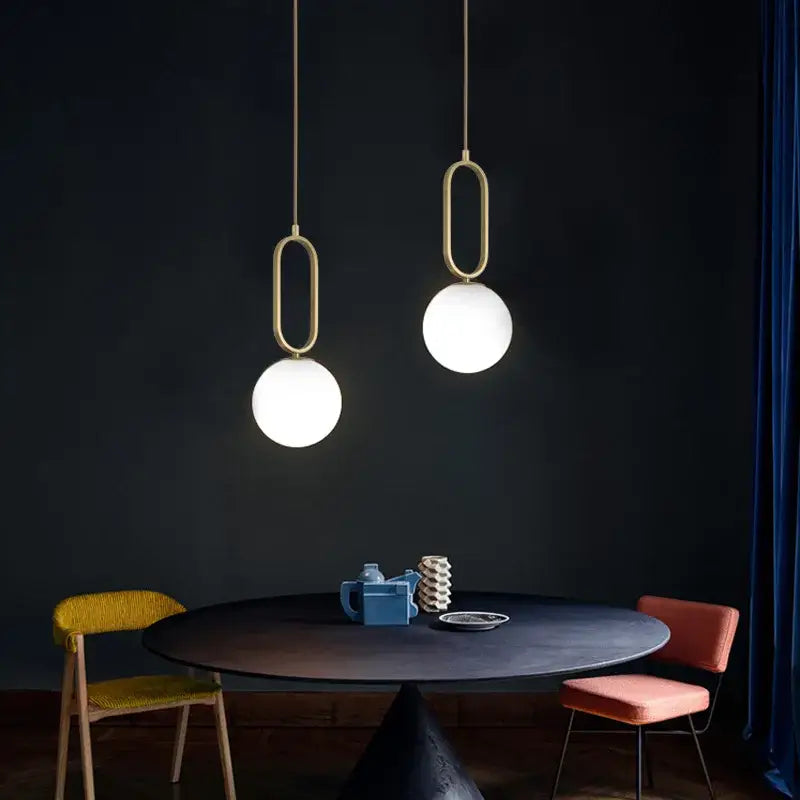 Two decorbites™ nordic pendant lights with gold metal frames and frosted glass ball light sources above a dark table