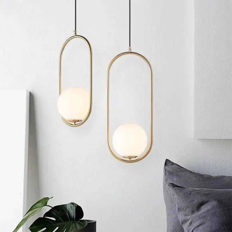 Two elegant DecorBites™ nordic gold pendant lights with frosted glass shade hang from black cords on white wall