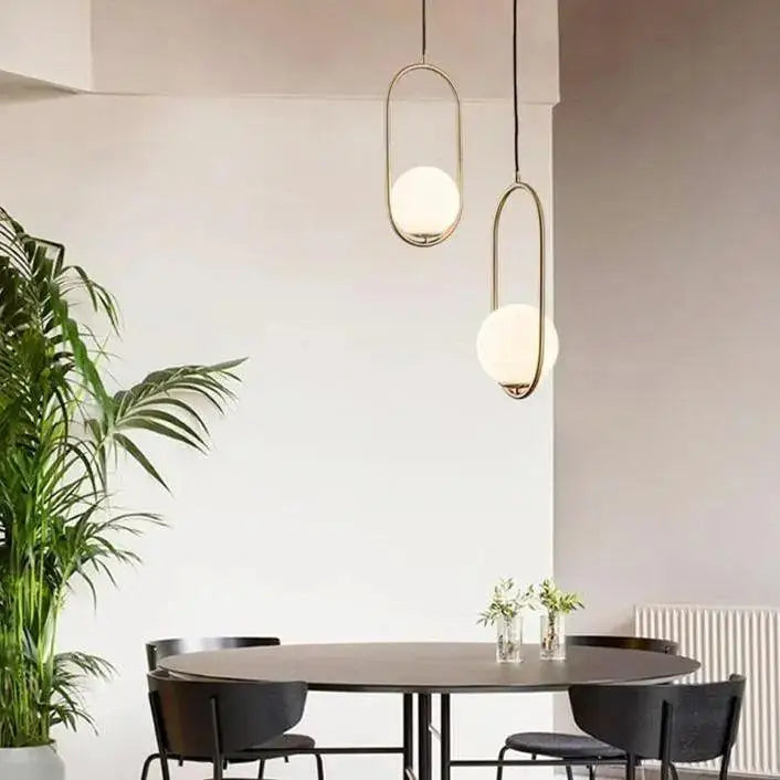 Two DecorBites™ nordic gold pendant lights with brass oval frames and white glass shades hang above a dining table