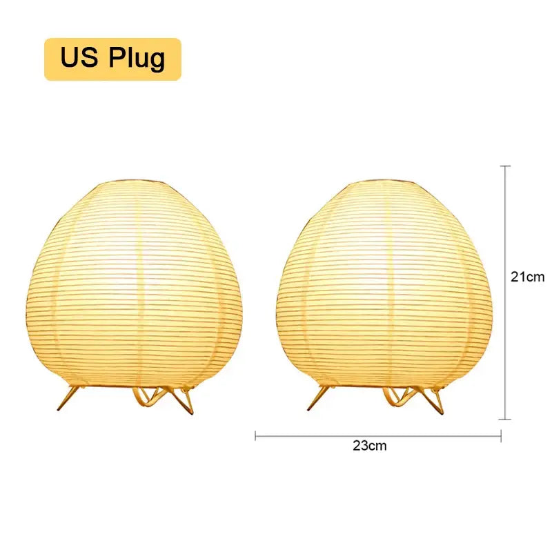Two warm yellow paper lantern led table lamps with gold metal stands measuring 21cm tall and 23cm wide for home decor