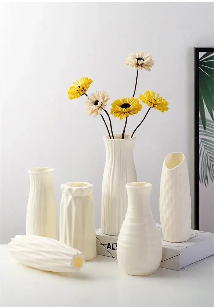 A collection of white nordic plastic vases with geometric designs holding yellow and cream flowers for modern decor