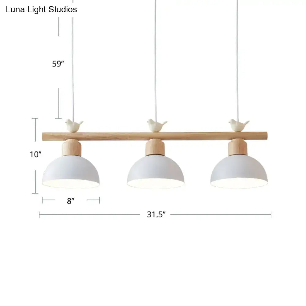 Minimalist three-light hanging island light with light wood bar, matte white metal shades, and ceramic bird decor