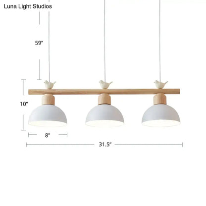 Minimalist three-light hanging island light with light wood bar, matte white metal shades, and ceramic bird decor