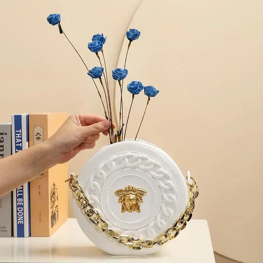 White circular handbag with gold chain strap and medusa head emblem in luxury fashion style nordic style flower vase half face