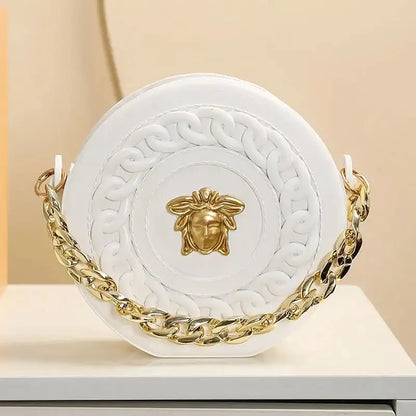 White circular handbag with gold-tone medusa head emblem and ornate chain strap displayed with nordic style flower vase