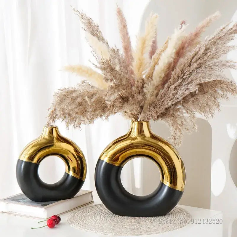 Two glossy black and gold ceramic nordic style circle vases holding dried pampas grass for flower arrangement