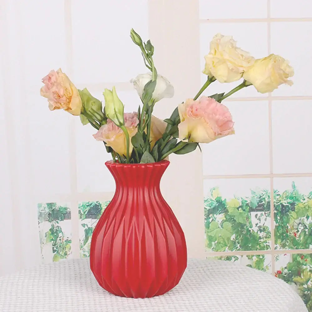 A vibrant red plastic flower vase with fluted geometric pattern holding soft pink and yellow roses for home decor