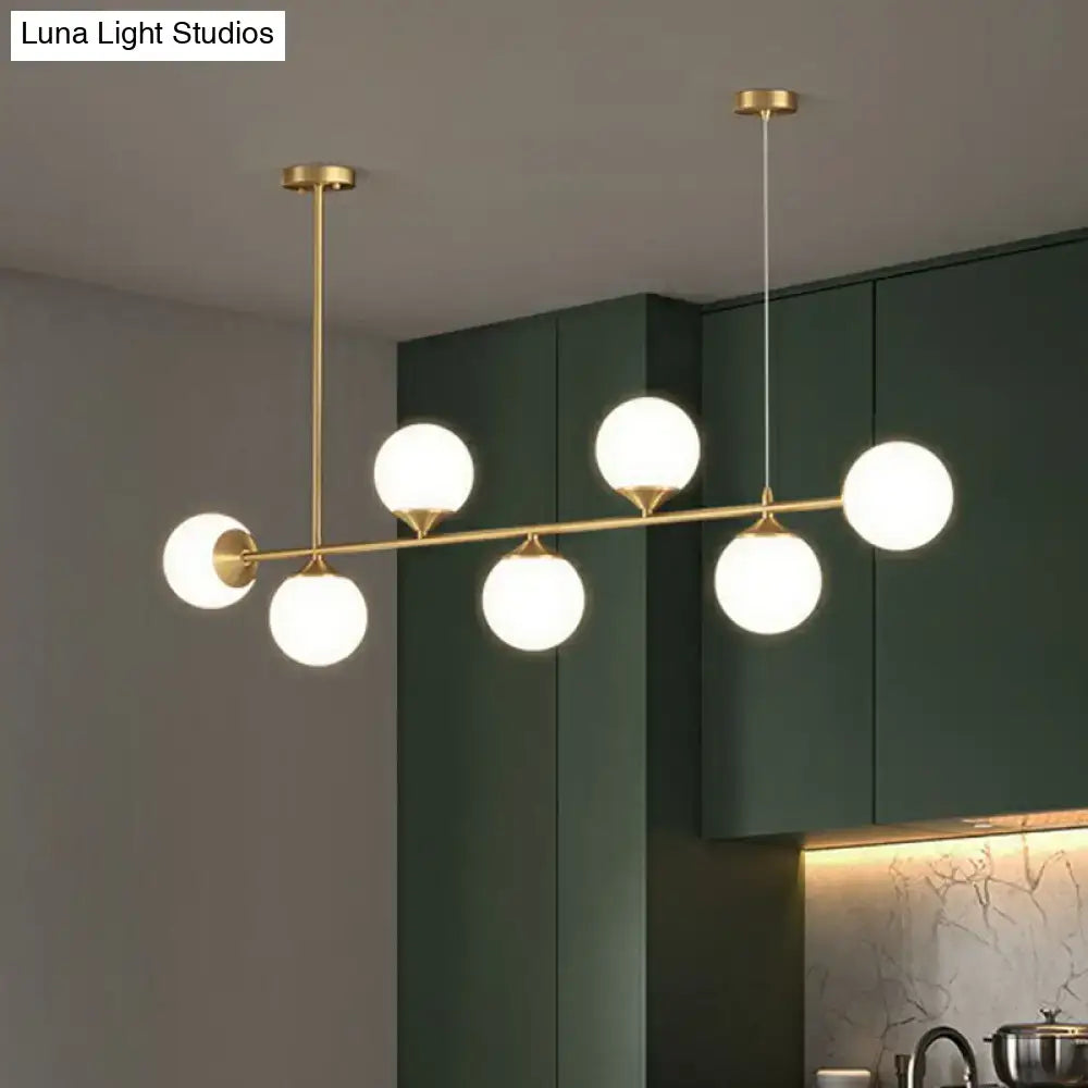 Modern brass pendant light with six frosted opaline glass globes designed for minimalist dining room island use