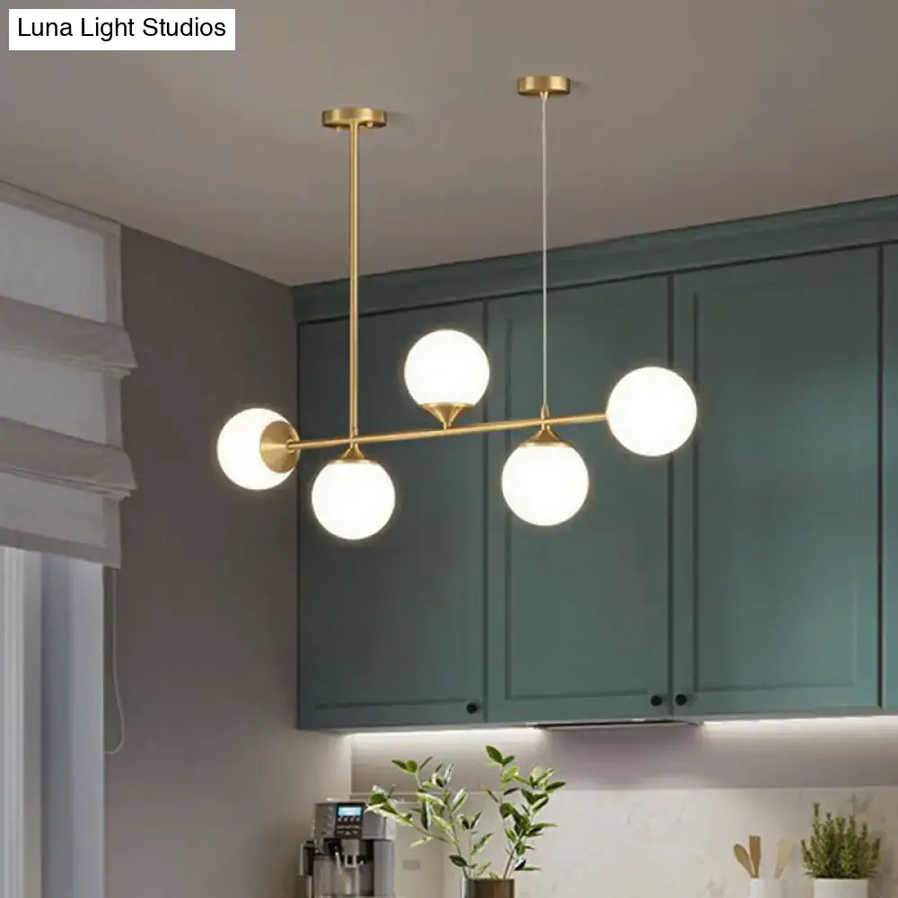 Modern brass pendant light with five frosted opaline glass globes for minimalist dining room island decor