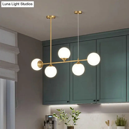 Modern brass pendant light with five frosted opaline glass globes for minimalist dining room island decor