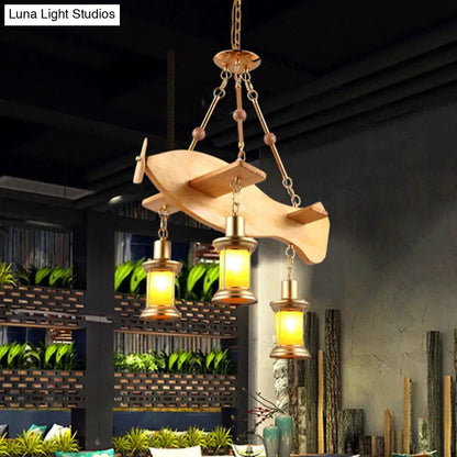 A rustic wooden airplane-shaped pendant light with brass accents and three orange glass lanterns featuring fish guitar design