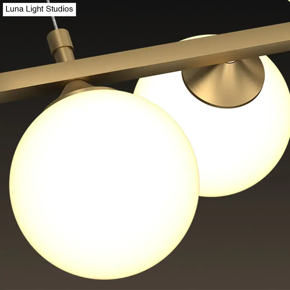 Modern brass-finished pendant light with two glowing white glass shade globes for postmodern restaurant use