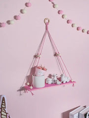 Pink green wooden macrame hanging shelf with wooden ring tassels holding white ceramic pot and miniature sheep for kids room