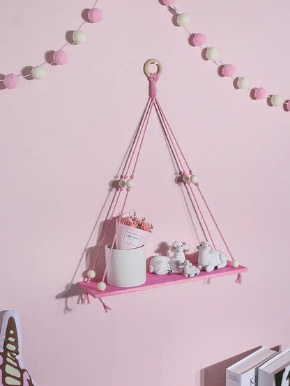 Pink green wooden macrame hanging shelf with wooden ring tassels holding white ceramic pot and miniature sheep for kids room