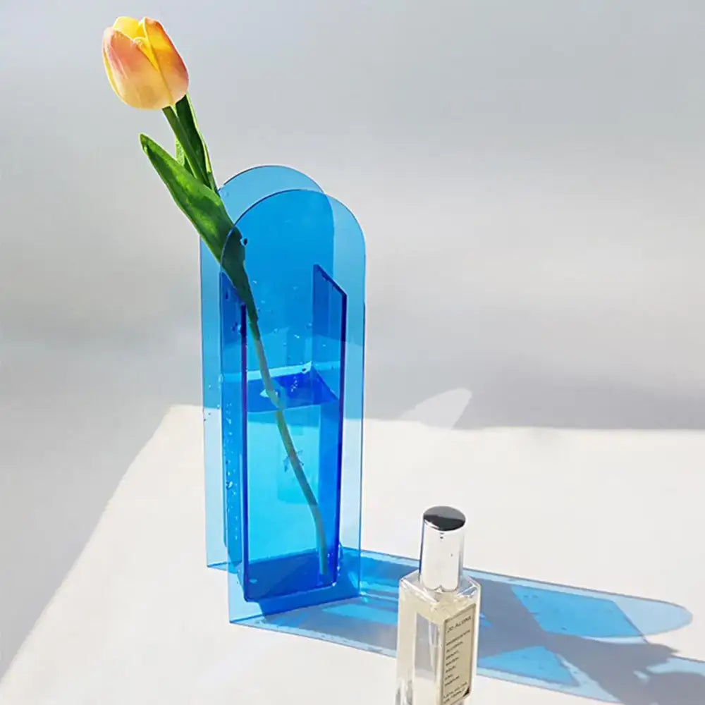 A translucent blue rainbow color acrylic flower vase in nordic style holding a single yellow-orange tulip