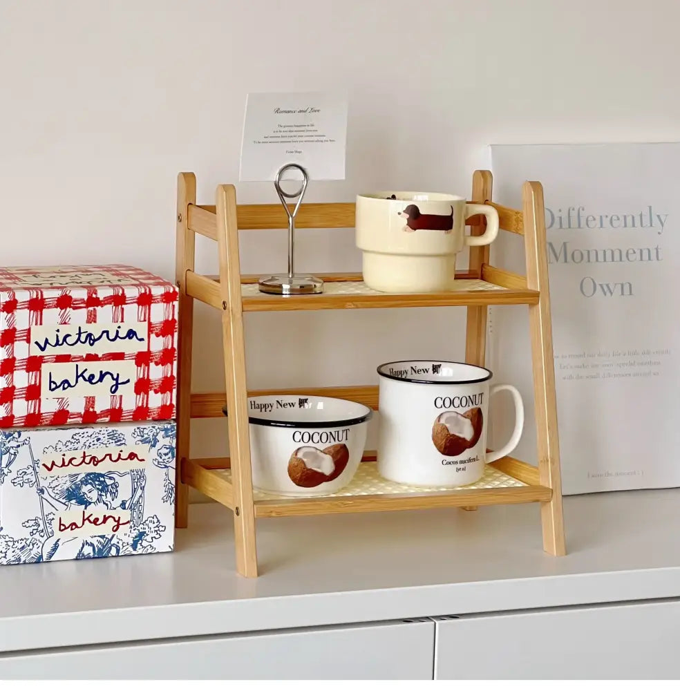 Light wood rattan two-tiered desktop organizer shelf with slatted design holding ceramic mugs and a card holder