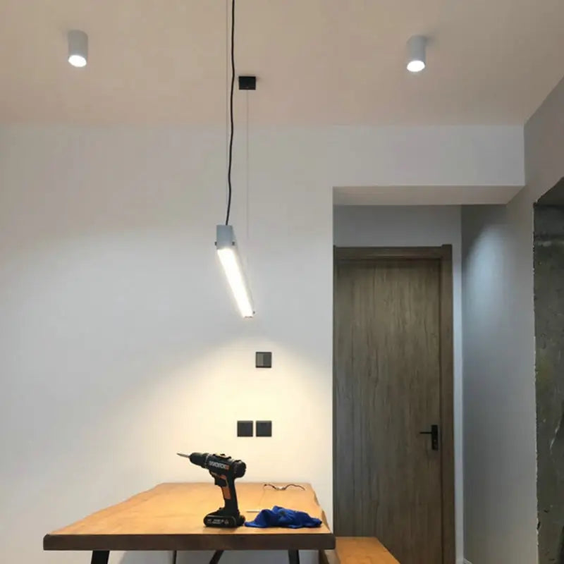 Black and orange cordless drill resting on a wooden table alongside decorbites led pendant light for dining room use