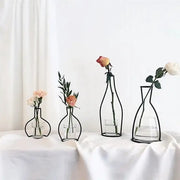 Black retro iron flower vase pot ornament with wireframe design and clear glass base holding single rose and greenery