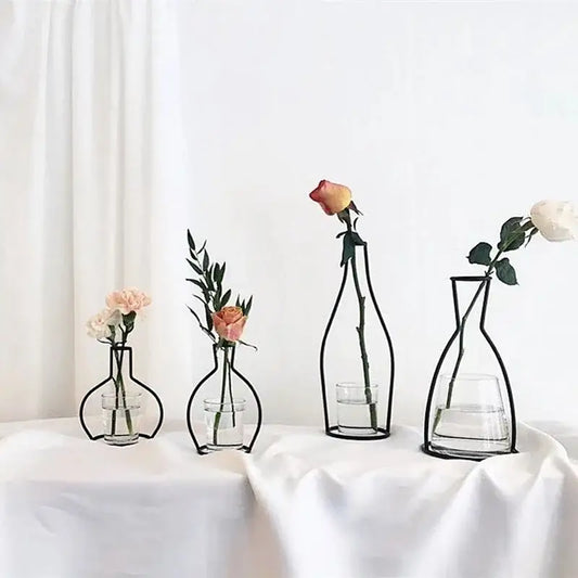 Black retro iron flower vase pot ornament with wireframe design and clear glass base holding single rose and greenery