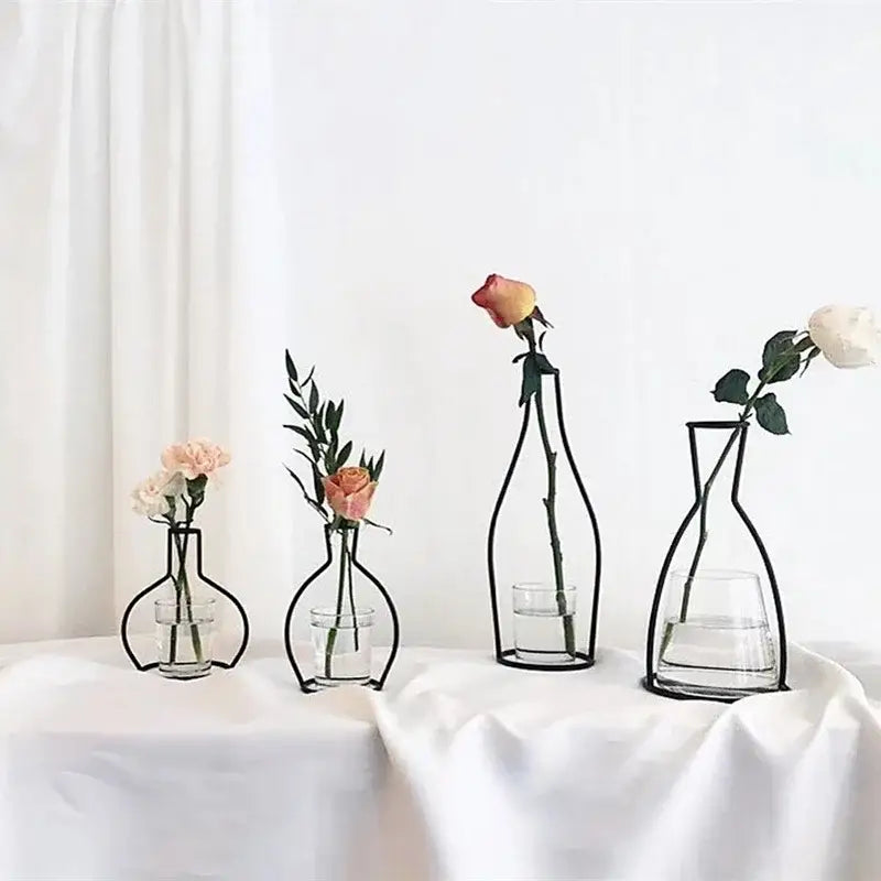 Black retro iron flower vase pot ornament with wireframe design and clear glass base holding single rose and greenery