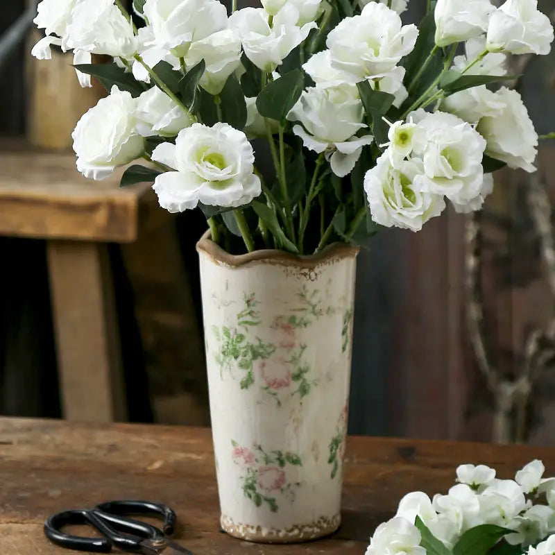 A cream-colored ceramic vase with scalloped rim and pink floral patterns holding white lisianthus in retro nordic ceramic style