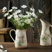 A rustic white ceramic vase with floral pattern and chipped glaze holding fresh daisies in retro nordic ceramic style