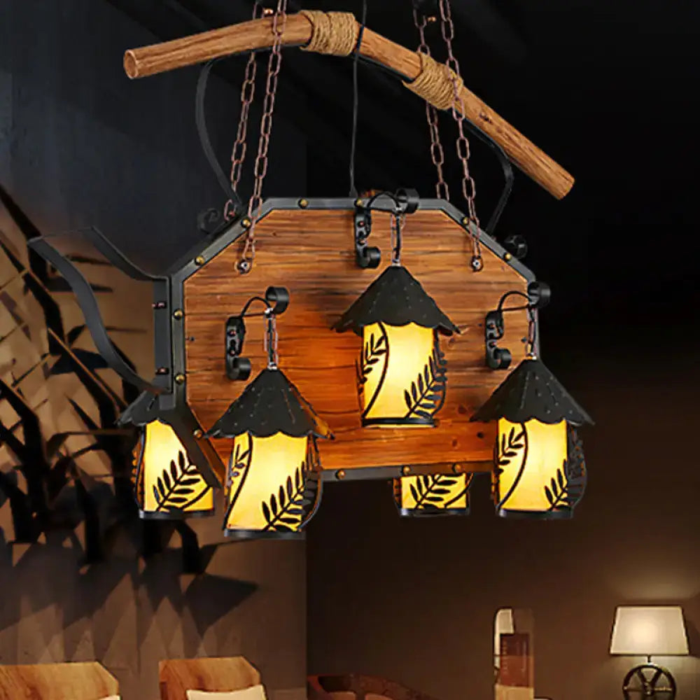 Rustic wooden chandelier with three amber glass lanterns featuring black leaf cutouts and clear glass shade chains