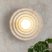 Decorbites round circle wall lamp is a rounded concrete wall sconce with concentric ridges and a warm glowing center