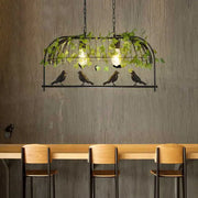 Black wrought iron birdcage island light fixture with illuminated bulbs and hanging green ivy for restaurant décor