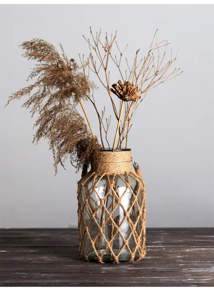 DecorBites™ rustic hanging glass vase wrapped in natural hemp rope holding dried pampas grass and branches
