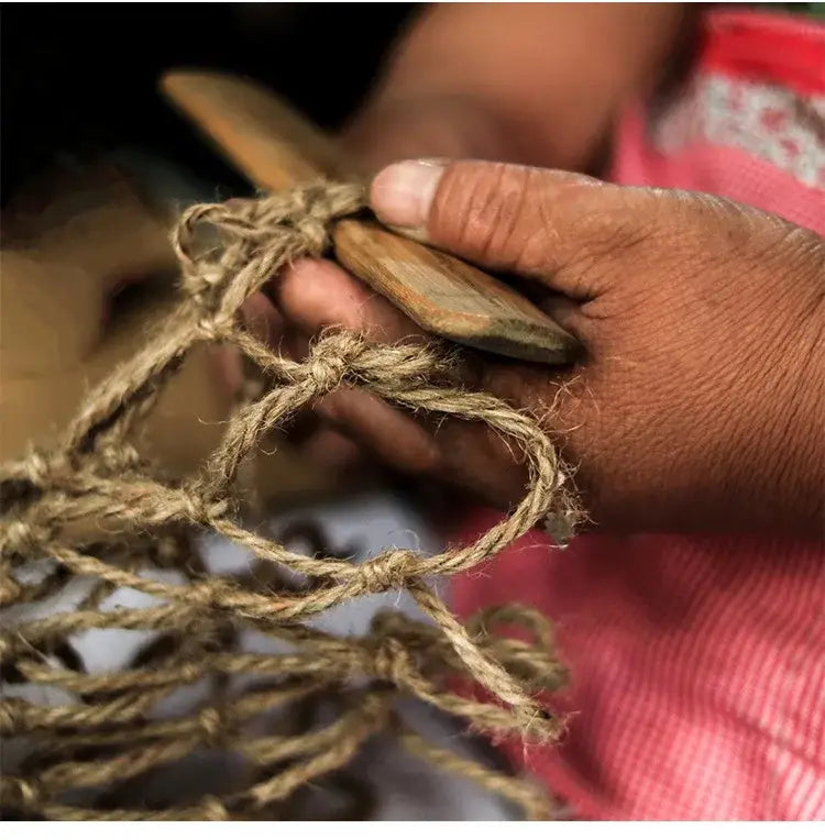 A hand holding a decorbites rustic hanging glass vase with a light brown hemp rope net and wooden tools