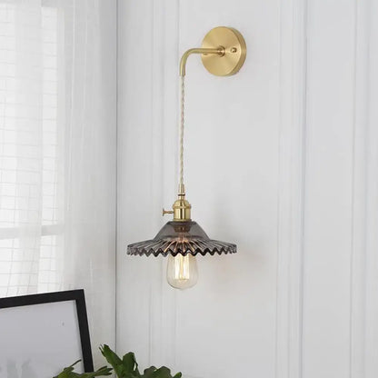 Industrial smoked glass brass sconce light with dark ribbed glass and exposed filament bulb for bedroom use